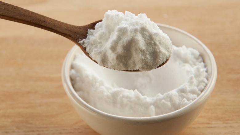 Person removing spoonful of baking soda from small bowl on table