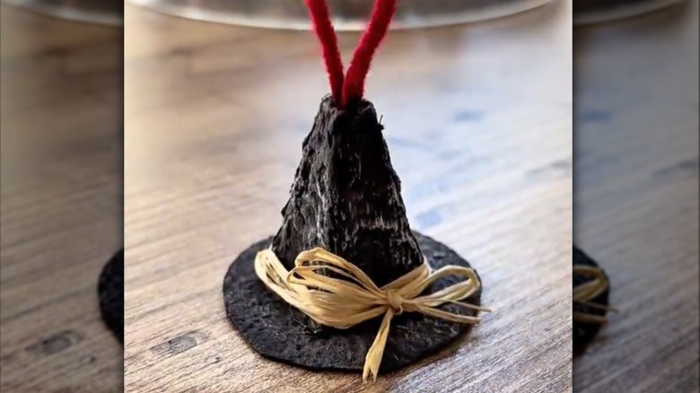 A small black DIY witch hat with red string coming out of the top made from an egg carton