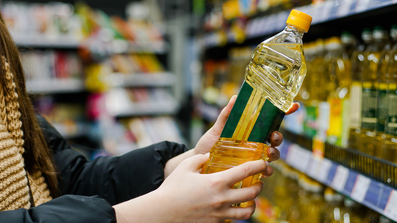 A person examines a bottle of vegetable oil by reading the label
