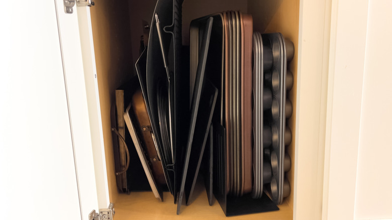 Cluttered metal pans and baking trays inside a kitchen cabinet