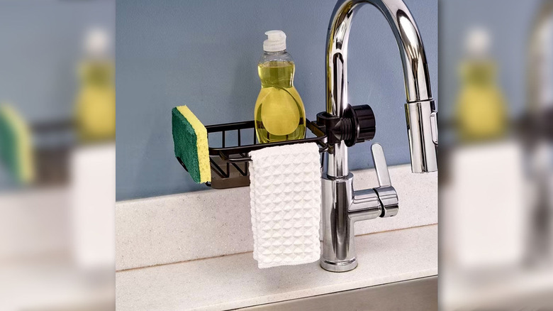 Kitchen caddy attached to silver sink faucet holding a sponge, dish soap and dish rag.
