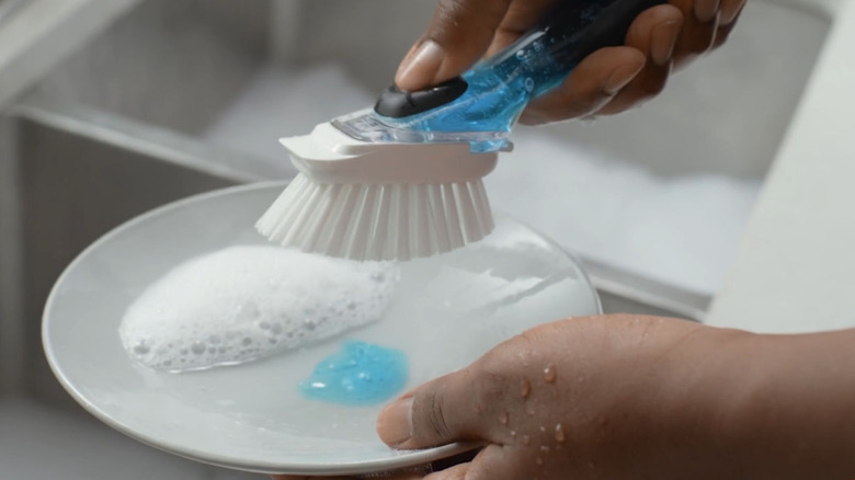 Dish brush with button to push for soap dispenser.