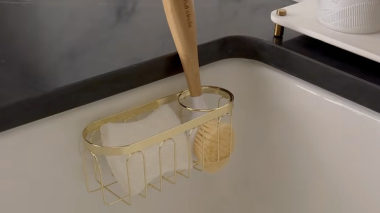 Gold sink caddy suctioned to inside of sink with sponge and dish brush inside.