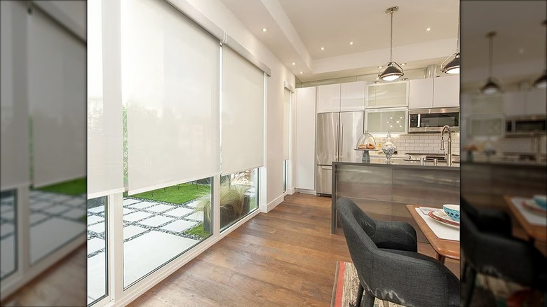 White solar roller shades in modern kitchen with hardwood floors, white cabinets, and metal island.