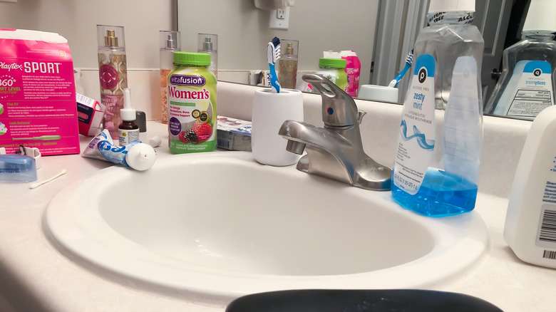 A messy bathroom counter with lots of clutter