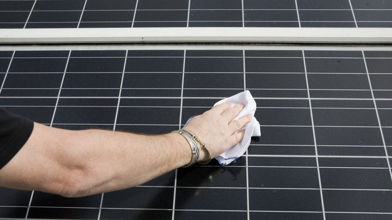 A man's hand holding a white cloth and wiping down a solar panel with it