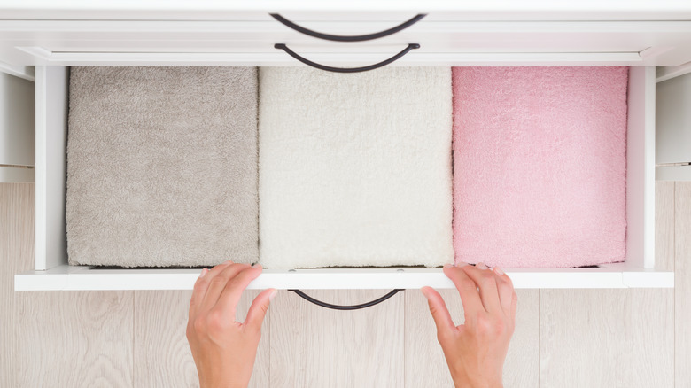 A person's hands and three towels neatly folded in a drawer