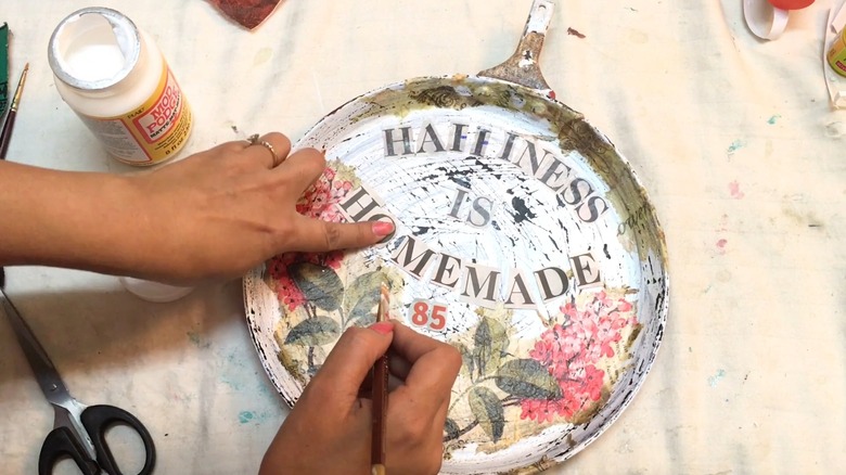 Person upcycling frying pan using decoupage and paint