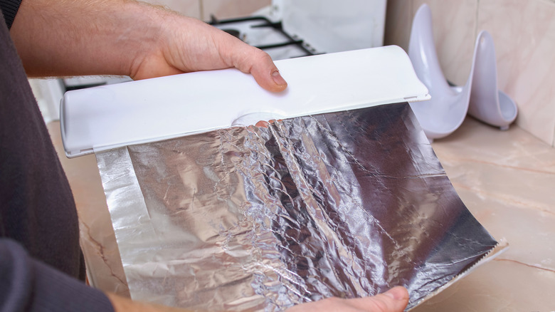 Hands unrolling aluminum foil