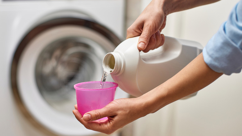 Person pouring transparent liquid detergent into plastic cap