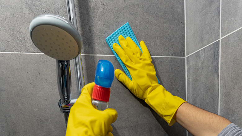 Closeup of person wearing yellow gloves cleaning the shower