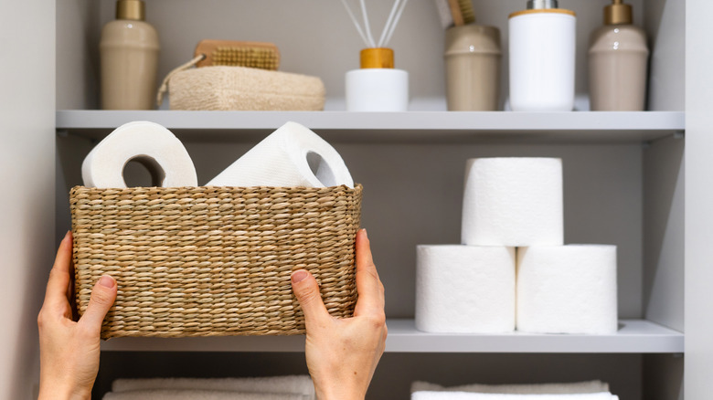 Person storing extra toilet paper in a basket in the linen closet