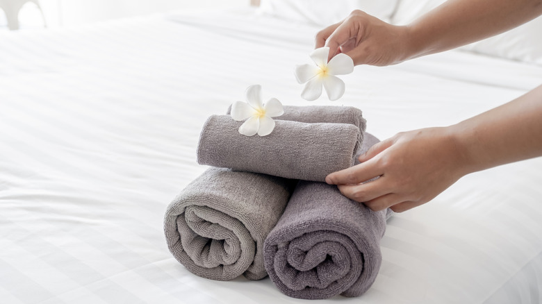 Hands place white flowers on a stack of fresh towels on a hotel bed.