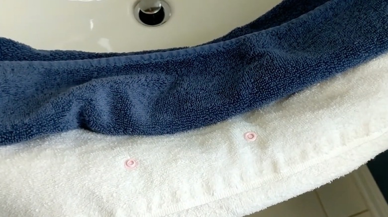 Pinks snaps attached to a white towel next to a blue folded towel