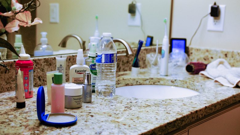 A bathroom countertop filled with beauty products, hygiene tools, and other clutter.