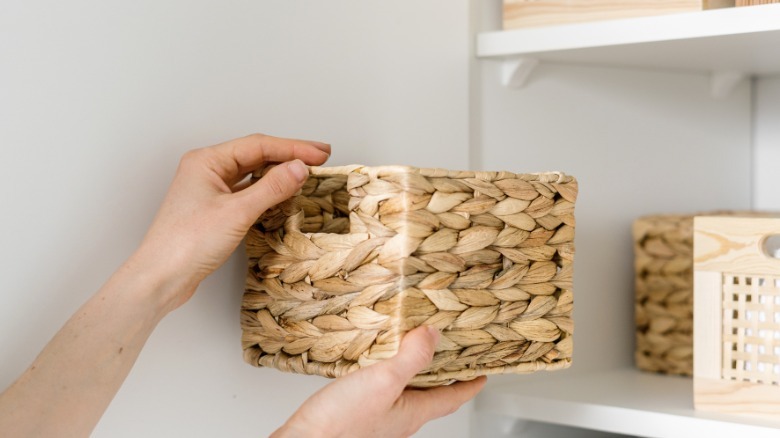 Person putting woven water hyacinth storage basket on closet shelf