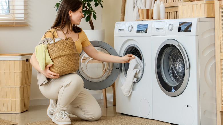 Woman putting in clothes from laundry hamper to washing machine