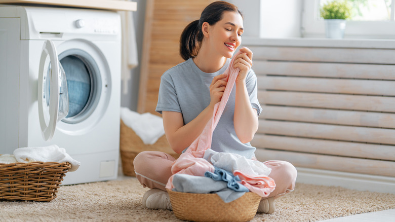 Woman smelling washed clothes and is sitting near washing machine