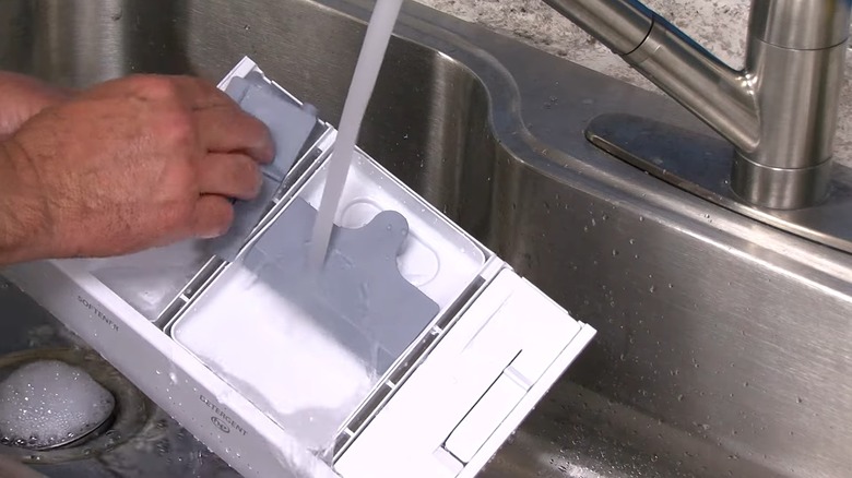 Hands washing a detergent drawer under running water