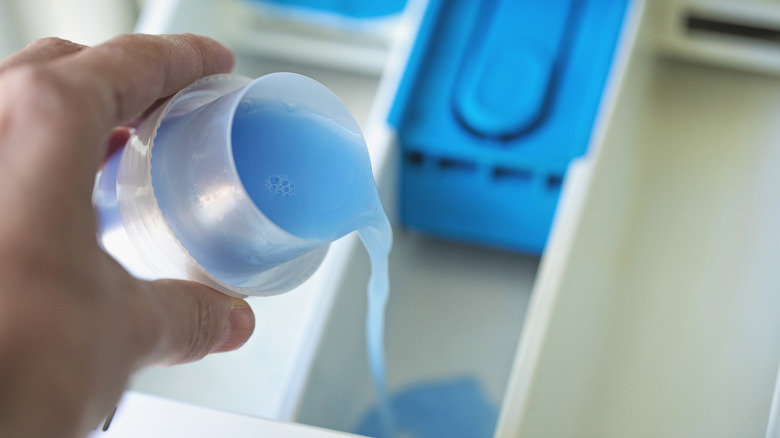 Hand pouring blue gel in a washer's compartment