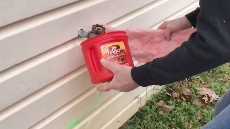 Person stuffing coffee can with pink insulation to cover faucet