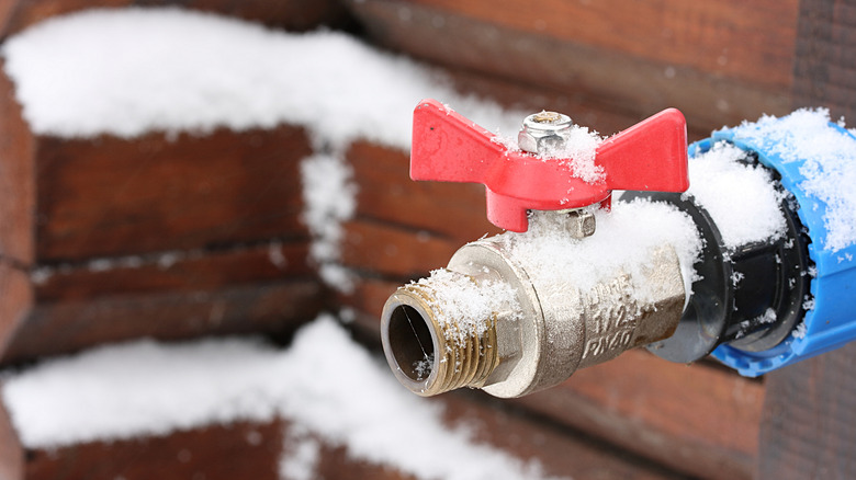 Snow-covered outdoor faucet on brick wall