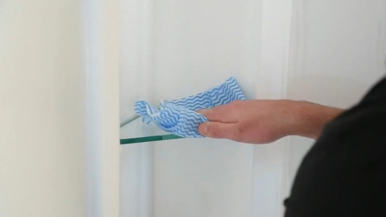 Man wiping glass shelf using a clean cloth