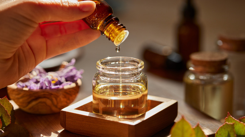 A person putting drops of essential oil in a glass jar