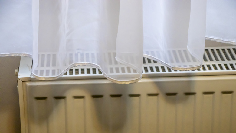 Sheer white curtains drape over the top of a radiator grate.