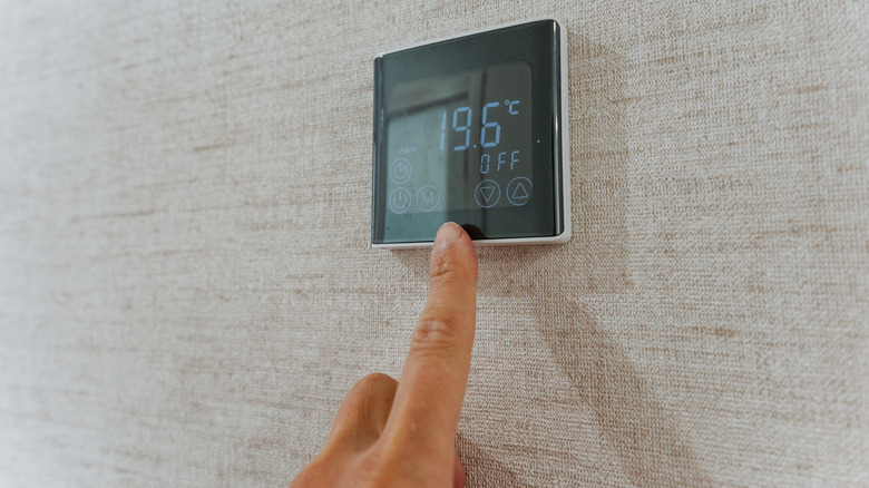 Close up of a hand touching a wall-mounted digital thermostat