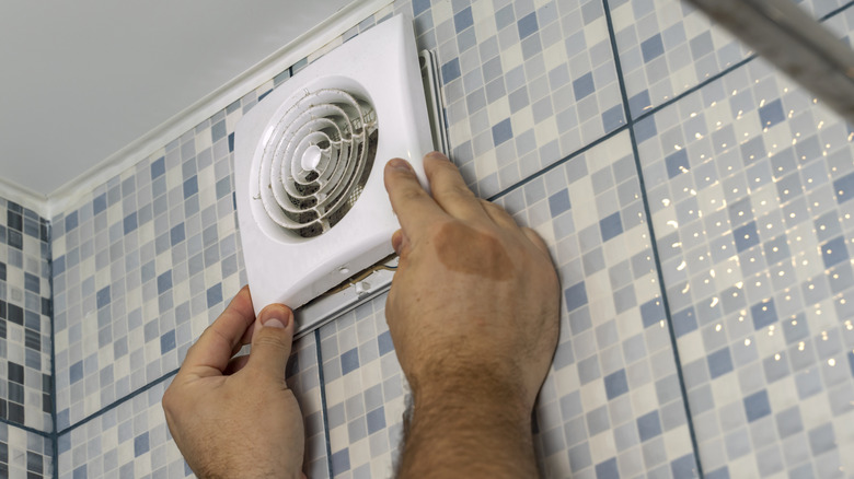 A close up of a person's hands installing a bathroom exhaust fan