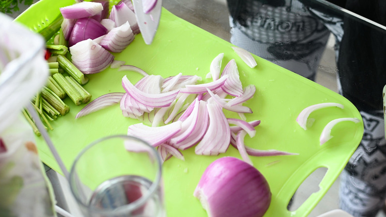 A red onion is chopped into strips on a green plastic cutting board.