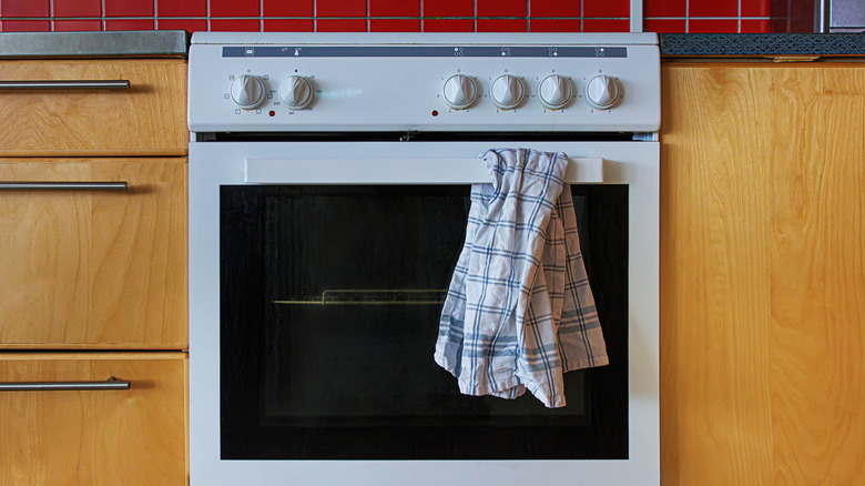 The front view of a white kitchen oven with control knobs and a plaid kitchen towel hanging from the handle.