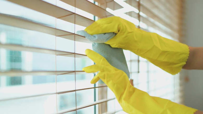 person in yellow gloves wiping down blinds with microfiber towel