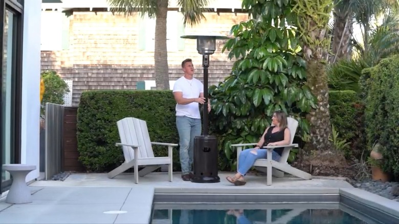Man positioning patio heater near seats by the backyard pool