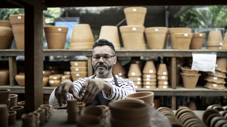 A man chooses some terracotta pots from among a large collection on shelves at a plant nursery.