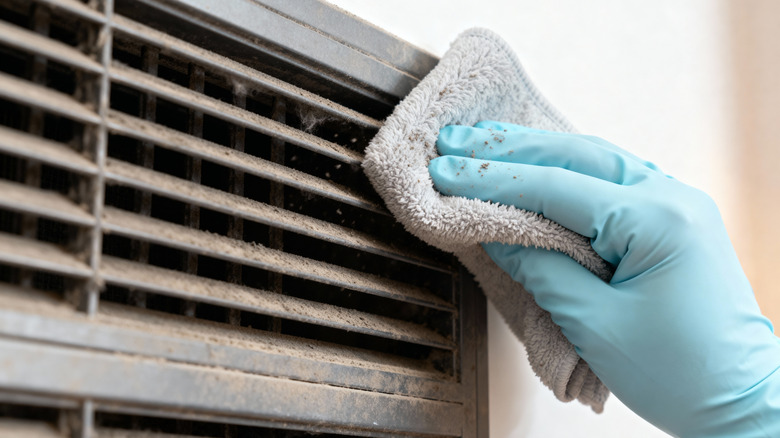 Person cleaning a dusty air vent with a cloth