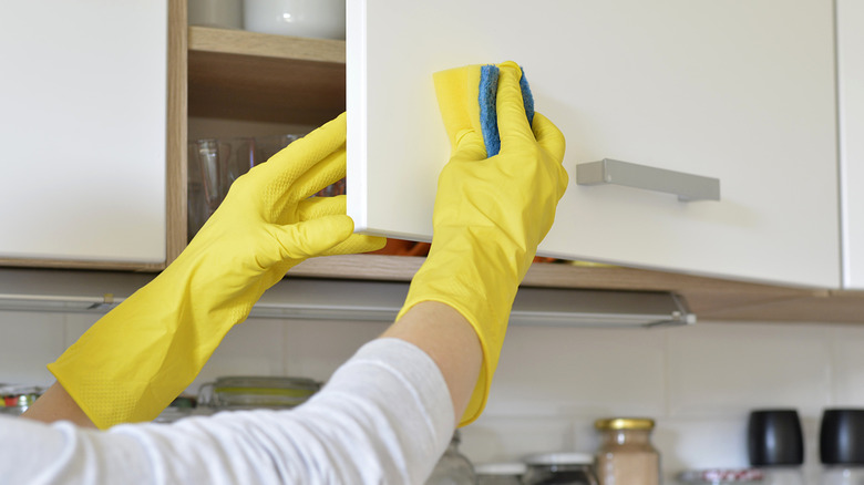Person wearing yellow rubber gloves cleaning cabinet door at home