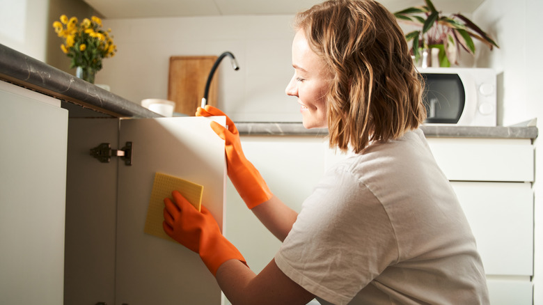 Portrait side view of the young woman wiping cabinets inside