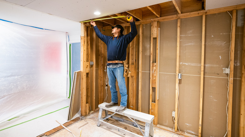 A tradesperson stands on a bench in the middle of a room that's being renovated.