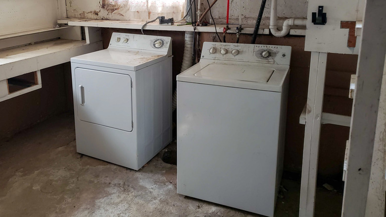 An old washer and dryer sit next to each other in a dingy basement.