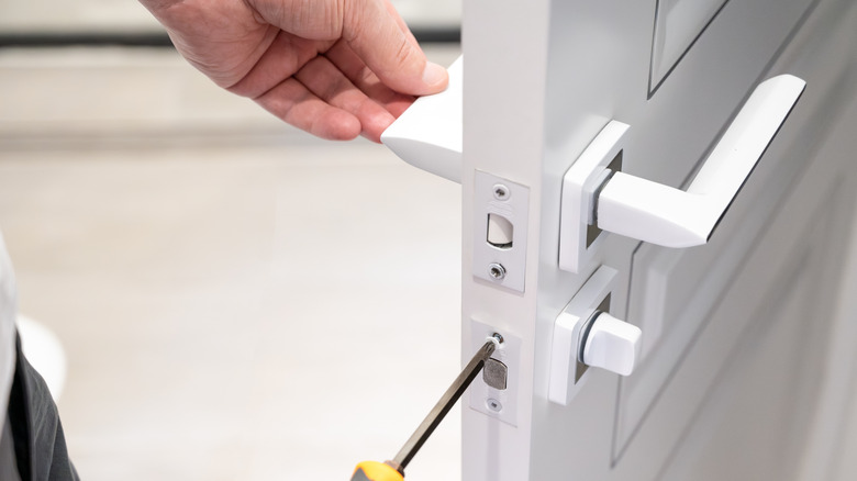 A person using screwdriver to install a door lock