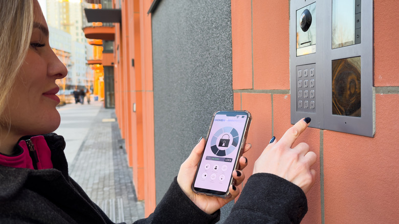 Woman unlocking smart entrance door lock with phone