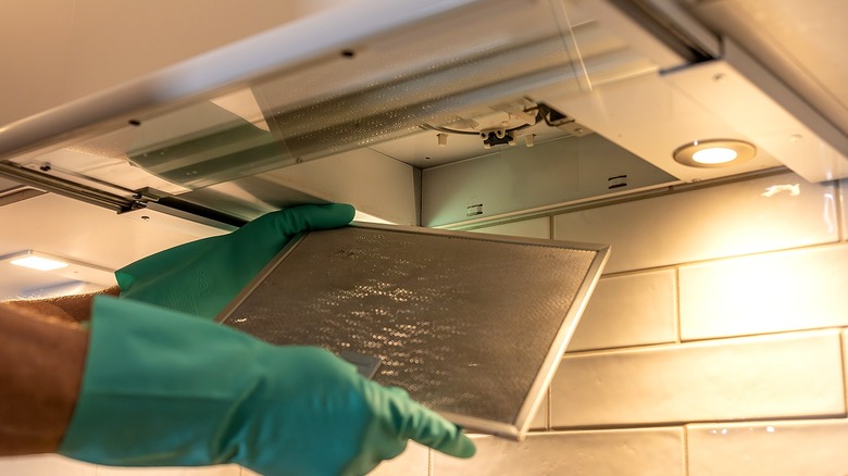 Gloved hands remove the filter from a range hood