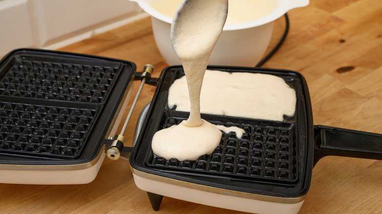Spoon pouring batter into a waffle maker