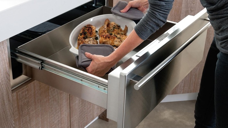 person putting platter of food in a warming drawer