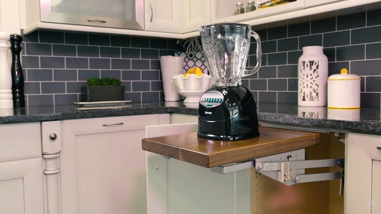 A blender sits atop a cabinet lift in a kitchen with a dark gray subway tile backsplash, black granite countertops, and white cabinets.