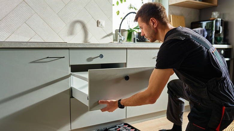 Man assembling kitchen drawer in modern cabinet using screwdriver.