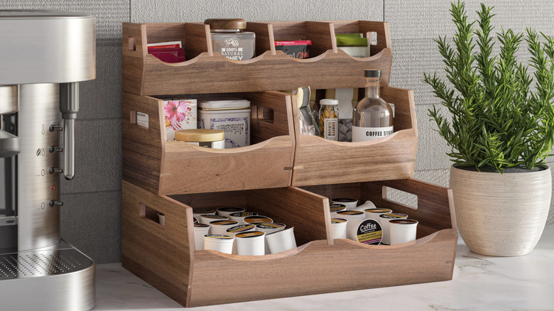 Seville Classics stacking bins holding tea, coffee cups, and sugar next to a coffee machine and a plant