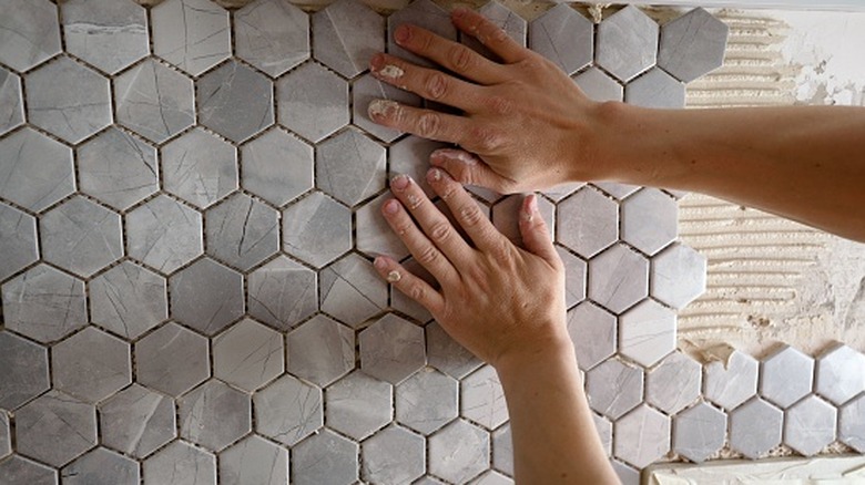 Hands pressing on hexagon tiles for a backsplash.
